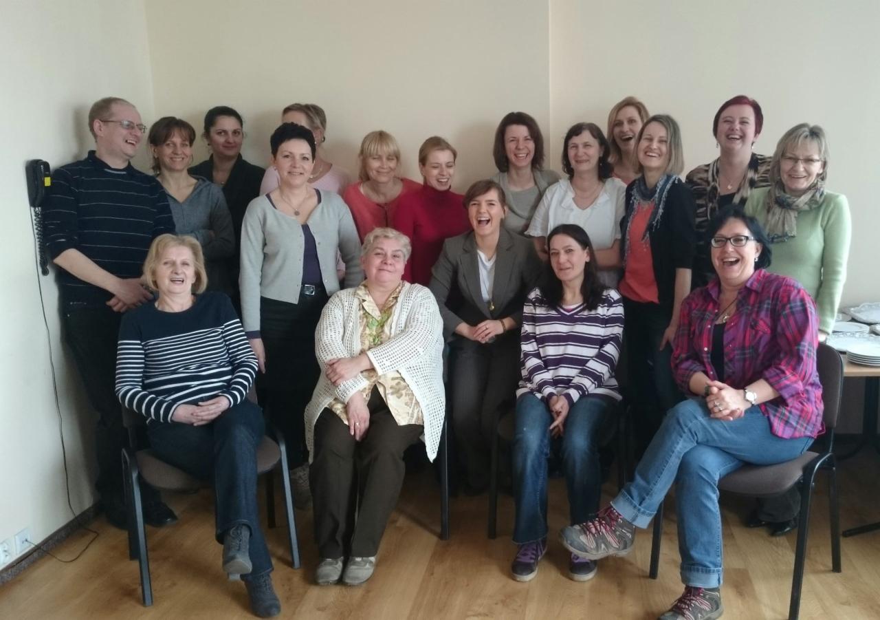 Grupa uśmiechniętych osób w różnym wieku, prawdopodobnie uczestnicy szkolenia lub kursu, pozujący do zdjęcia grupowego w jasnym pomieszczeniu.