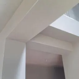 Wnętrze z wykonanymi zabudowami z płyt gipsowo-kartonowych, widoczne proste linie i kąty, ściany pomalowane na biało, surowy stan wykończenia.