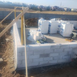 Murtechnik Paweł Żurek - Wznoszenie ścian fundamentowych z bloczków Solbet. Widoczne narzędzia, poziomica i zapas materiałów budowlanych. Prace murarskie w toku, zarys przyszłego budynku.