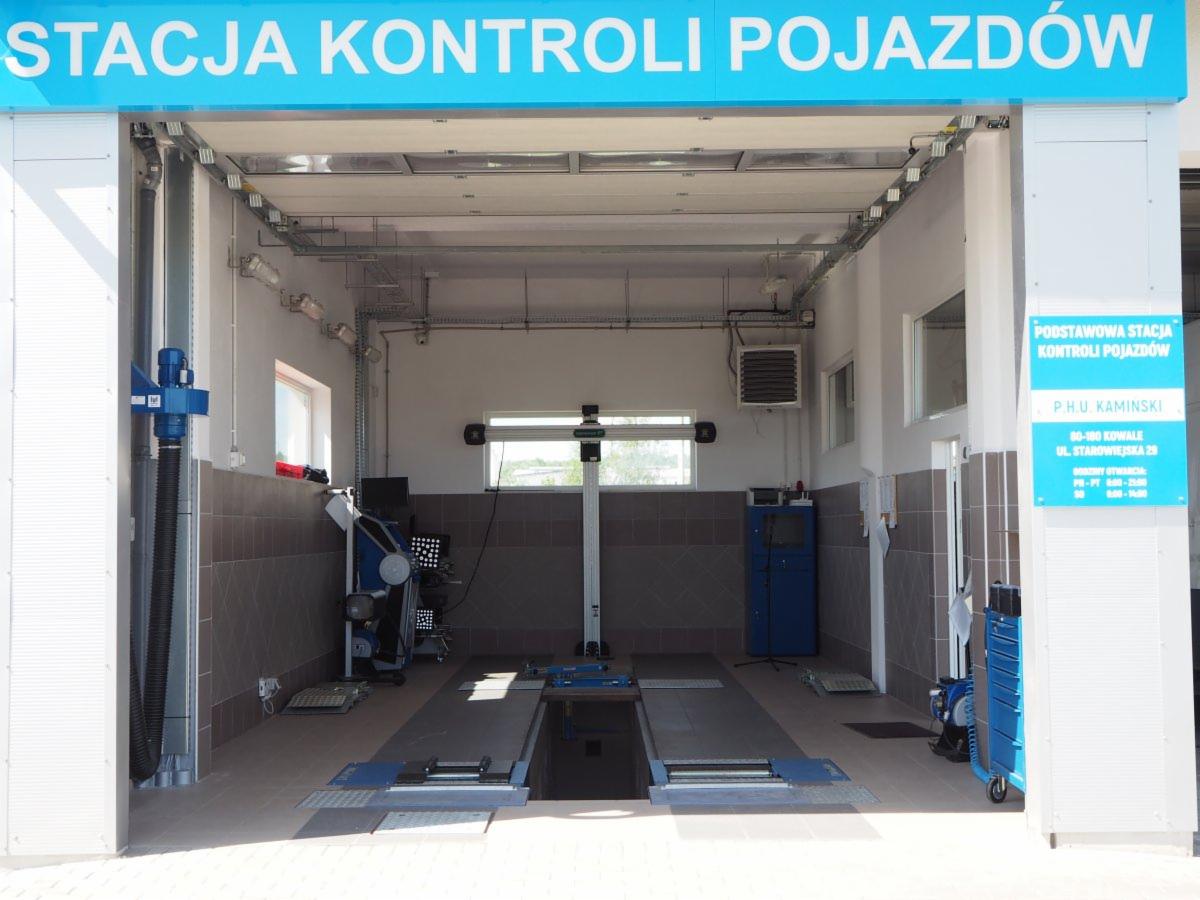 Wnętrze stacji kontroli pojazdów z kanałem diagnostycznym, urządzeniem do geometrii kół i niebieskim wózkiem narzędziowym.