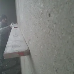 Pracownik z Kępna przykłada poziomicę do świeżo nałożonego tynku na ścianie, kontrolując równość powierzchni.