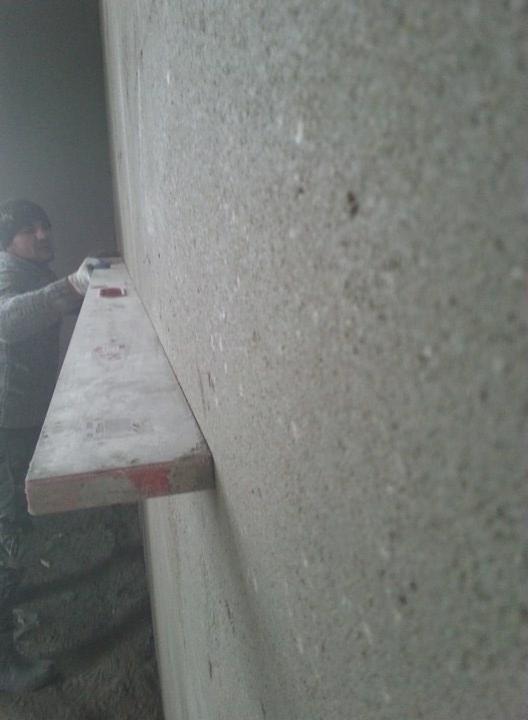 Pracownik z Kępna przykłada poziomicę do świeżo nałożonego tynku na ścianie, kontrolując równość powierzchni.