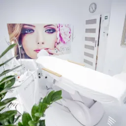 Jasne wnętrze gabinetu kosmetycznego z fotelem do zabiegów, urządzeniem Biotec Italia i plakatem z wizerunkiem kobiety.