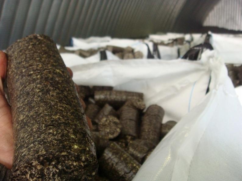 Ręka trzyma agropellet na tle worka wypełnionego pelletem w magazynie z blachy falistej.