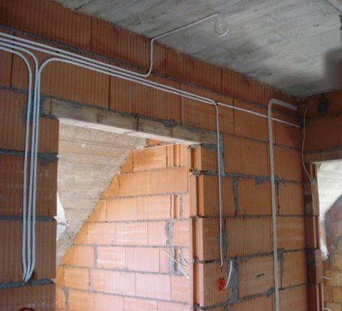 Instalacja elektryczna natynkowa w nowo wznoszonym budynku z cegły ceramicznej, widoczne białe kable prowadzone po ścianach i suficie, brak tynków.