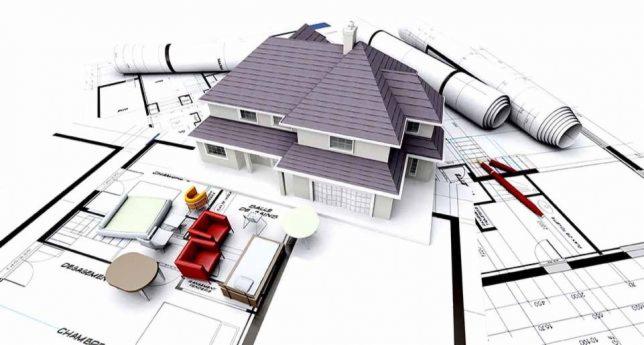 Model dwukondygnacyjnego domu z szarym dachem, umieszczony na planach architektonicznych z meblami w miniaturze i zwiniętymi rysunkami w tle.