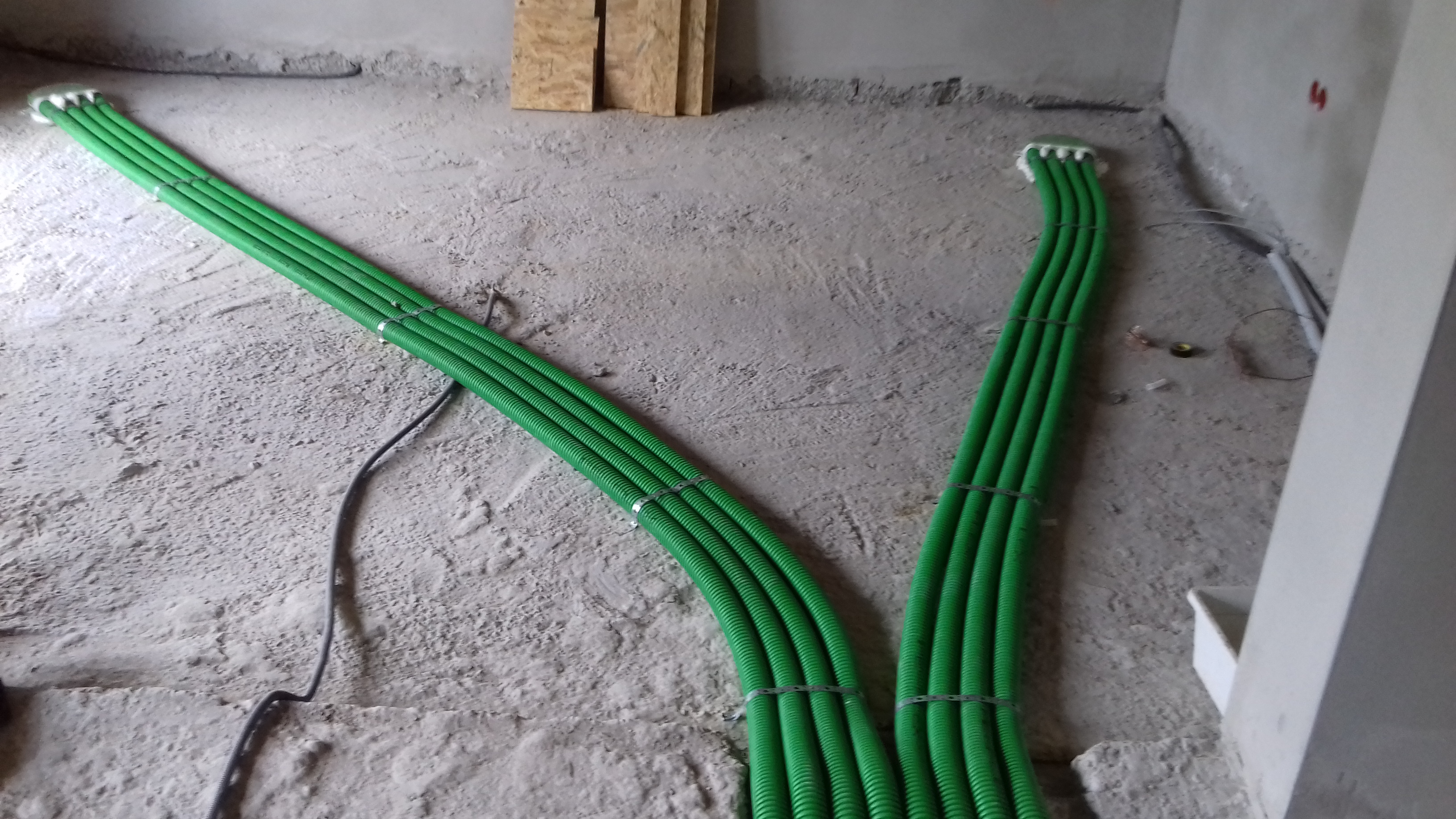 Zielone rury wentylacyjne ułożone w wiązki na surowym betonowym podłożu w trakcie montażu instalacji.