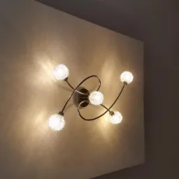 Świecąca, nowoczesna lampa sufitowa z pięcioma szklanymi kloszami w kształcie kuli, zamontowana na białej ścianie, z widocznym fragmentem szarej ściany po prawej stronie.