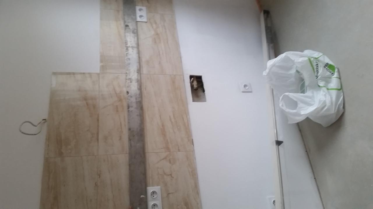 Przygotowanie do montażu gniazdek elektrycznych w nowo wykończonej łazience z beżowymi płytkami imitującymi marmur, widoczne puszki instalacyjne i przewody, ślady po montażu listwy maskującej.