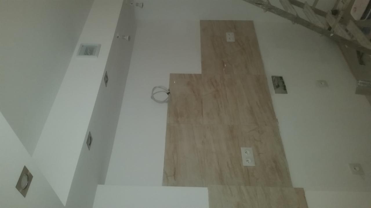 Wnętrze w trakcie prac wykończeniowych: widoczne kable elektryczne wystające ze ściany obok fragmentu dekoracyjnej okładziny ściennej imitującej marmur, gniazdka elektryczne oraz otwory...