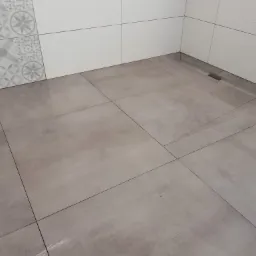 Wykończona łazienka z szarymi płytkami podłogowymi i białymi płytkami ściennymi, w rogu widoczny odpływ liniowy.