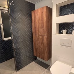 Wood House Group - Nowoczesna łazienka z ciemną, ułożoną w jodełkę glazurą pod prysznicem, drewnianą szafką wiszącą i białą toaletą. Minimalistyczny design, szare płytki podłogowe.