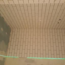 Wood House Group - Ściana i sufit w trakcie układania białych, podłużnych płytek. Widoczny zielony laser wyznaczający linię. Część ściany pokryta płytą gipsowo-kartonową.