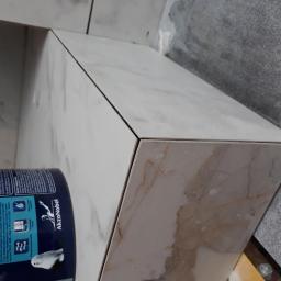 Wood House Group - Półka wnękowa wykończona płytkami imitującymi marmur, z widocznym narożnikiem i tubą farby AkzoNobel, w trakcie prac wykończeniowych.