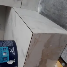 Półka wnękowa wykończona płytkami imitującymi marmur, z widocznym narożnikiem i tubą farby AkzoNobel, w trakcie prac wykończeniowych.