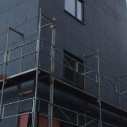 Wood House Group - Elewacja budynku wielopiętrowego w trakcie montażu, z widocznymi rusztowaniami i panelami elewacyjnymi w odcieniach szarości.