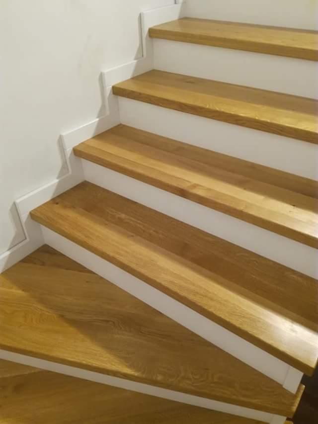 Wykończone drewniane schody z jasnego dębu z białymi podstopnicami i listwami, widok z dołu, prezentujące naturalne usłojenie drewna i minimalistyczny design.