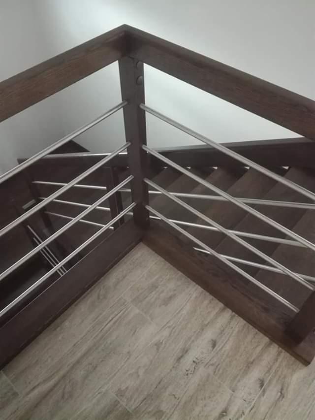 Schody wykończone ciemnym drewnem z metalowymi poręczami, widok z góry na narożnik, parkiet imitujący drewno na podłodze.