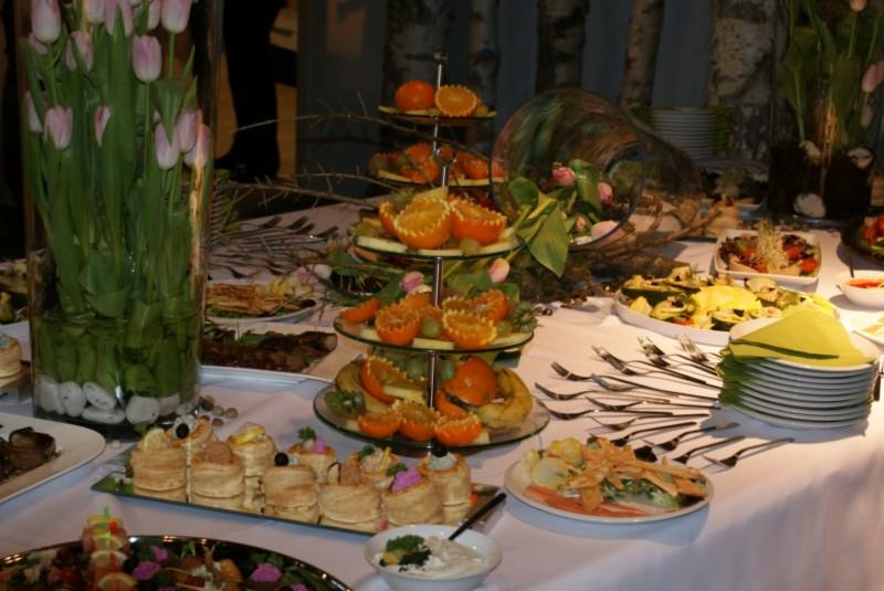 Bogato zastawiony stół z dekoracjami kwiatowymi, paterą z owocami, kanapeczkami i sałatkami podczas przyjęcia.