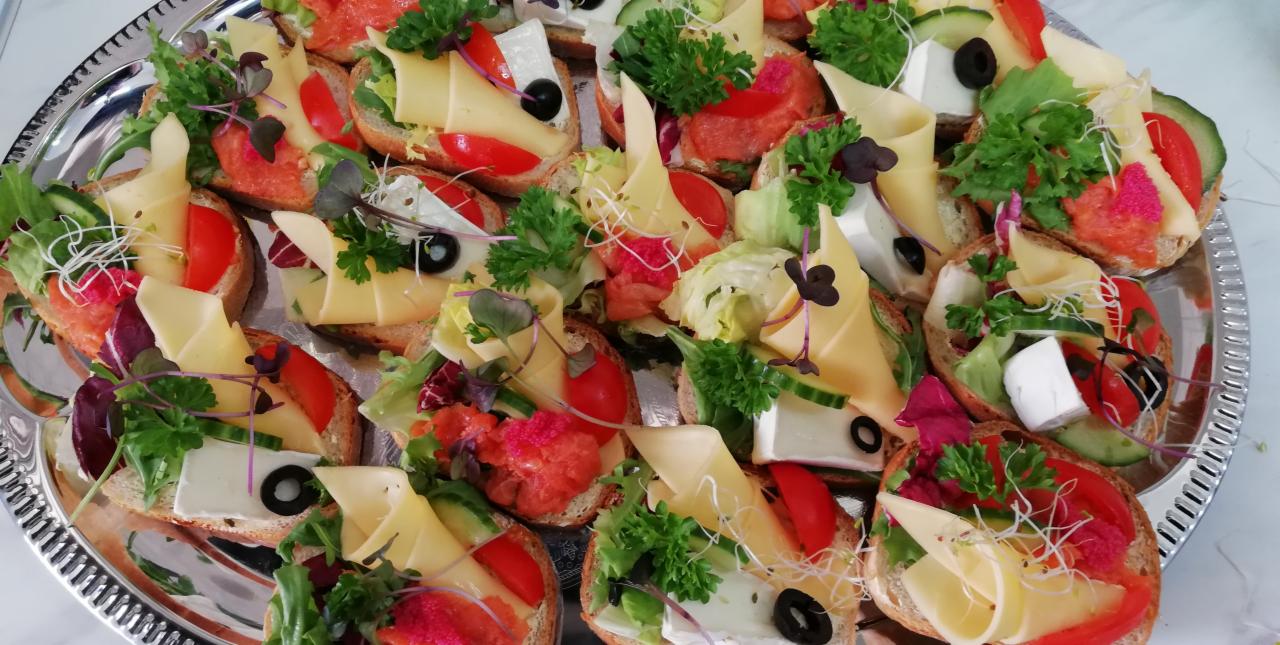 Srebrna taca z różnorodnymi kanapkami na pieczywie, udekorowanymi serem, warzywami, ziołami i oliwkami, z bliska.