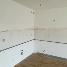 Fragment ściany w trakcie układania płytek w kuchni, widoczne profile montażowe, zaznaczone linie fug, oraz przygotowane podłączenia hydrauliczne.