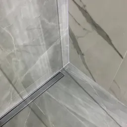 Szary marmurkowy wzór płytek w rogu kabiny prysznicowej z odpływem liniowym Hansgrohe.