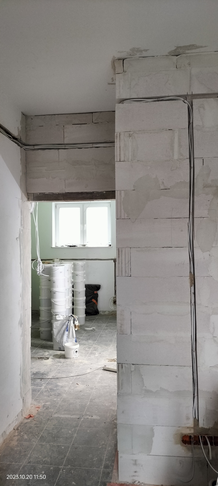 Wnętrze w trakcie remontu: widoczne przewody elektryczne prowadzone po ścianie z bloczków, w tle ustawione wiadra z farbą i torba budowlana.