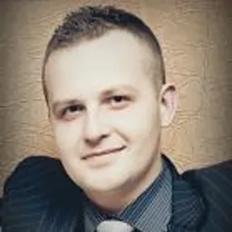 Młody mężczyzna w garniturze w prążki, z lekko uśmiechniętą twarzą, na rozmytym tle w ciepłych odcieniach brązu. Portret w biznesowym stylu.