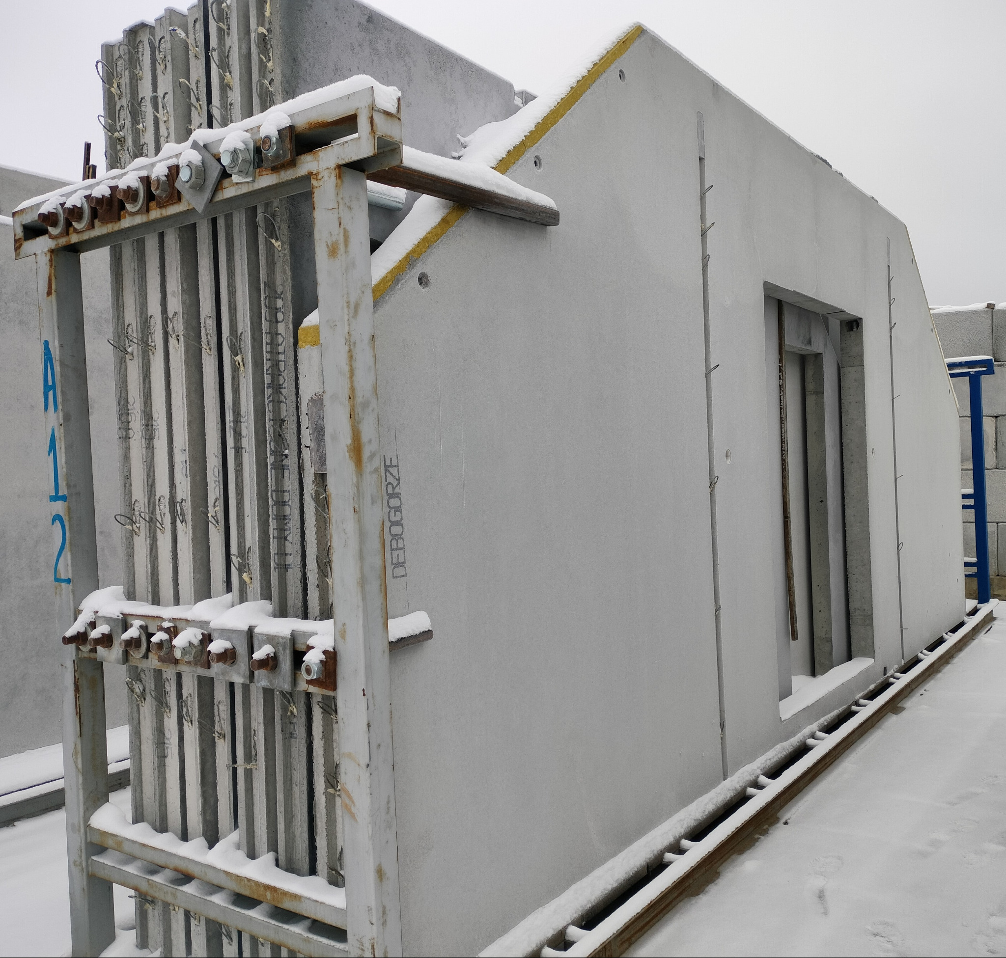 Prefabrykowane elementy domu modułowego, pokryte śniegiem, przygotowane do transportu na plac budowy. Widoczne detale łączeń i izolacji.