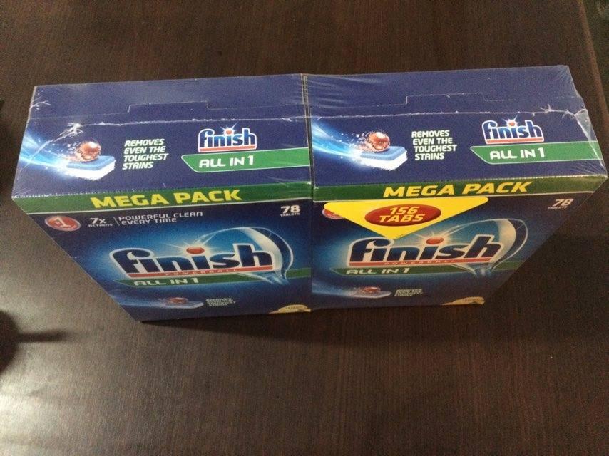 Dwa opakowania zbiorcze tabletek do zmywarki Finish All in 1, jedno z naklejką 156 tabs, drugie 78, zafoliowane i ułożone na ciemnym blacie.
