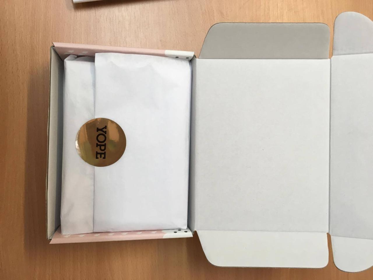 Otwarta, różowa pudełko z białymi gwiazdkami, wewnątrz zawartość owinięta w biały papier z naklejką 'YOPE', widoczne wnętrze pudełka.