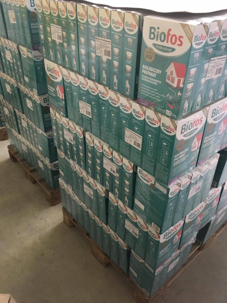 Palety z ułożonymi w stos kartonami z biologicznym preparatem Biofos Professional, widoczne etykiety i logo producenta.