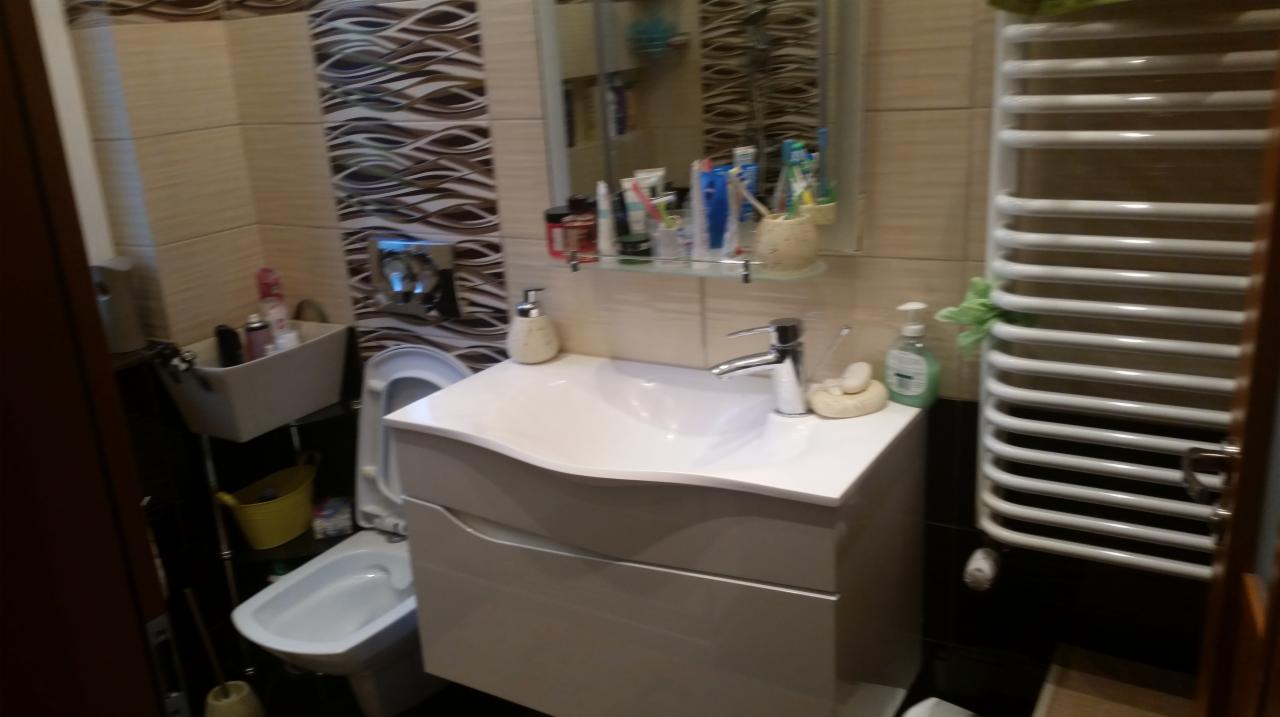 Jasna łazienka po remoncie z umywalką z szafką, bidetem i grzejnikiem drabinkowym, płytki imitujące fale na ścianie.