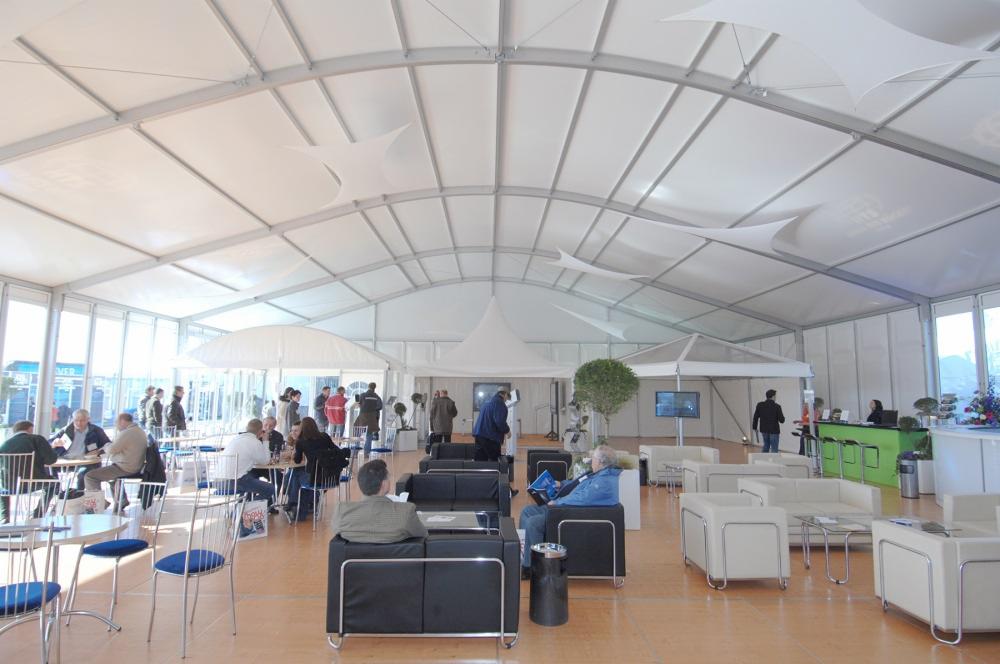 Wnętrze przestronnej hali namiotowej z metalową konstrukcją, wyposażonej w stoliki, krzesła i sofy dla gości.