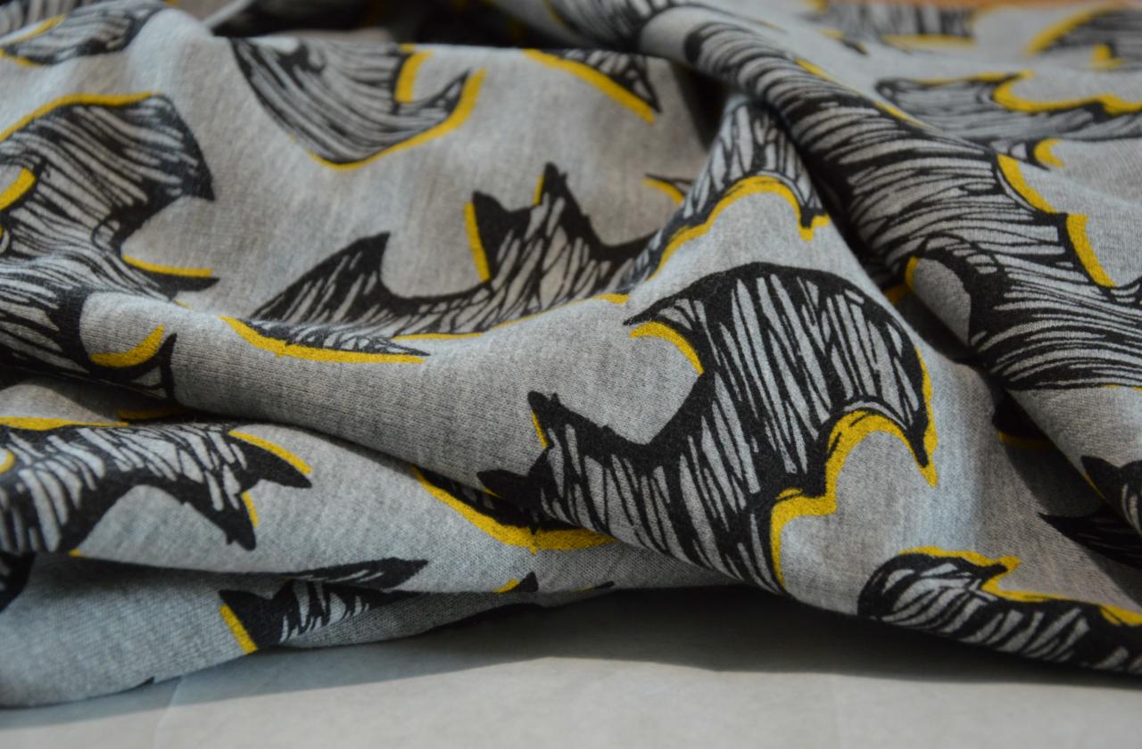 Fałdy szarej dzianiny z czarno-żółtym wzorem nietoperzy, widoczne zbliżenie na fakturę materiału.