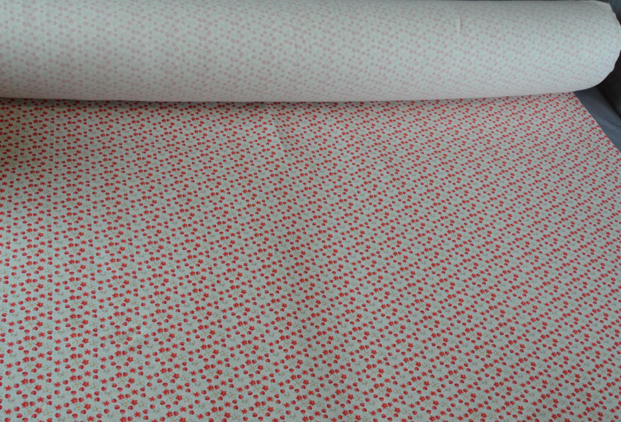 Rolka jasnej tkaniny w drobne czerwone kwiatki i beżowe kropki, widoczny fragment rozwiniętej tkaniny.