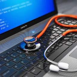 Laptop 'Laptop Pro' z niebieskim ekranem błędu, na klawiaturze leży pomarańczowo-srebrny stetoskop.