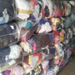 Stos zapakowanych w folię transparentną paczek z odzieżą, zabezpieczonych brązową taśmą, ułożonych jedna na drugiej.