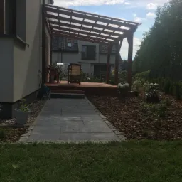 Nowoczesny ogród przydomowy z drewnianą pergolą, tarasem i kamienną ścieżką, wykończony korą i zielenią.