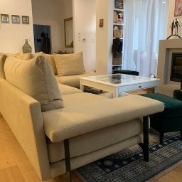 TOPMEBLE - MEBLE TAPICEROWANE ANDRZEJ ZALEWSKI - Jasna, narożna sofa z beżową tapicerką i metalowymi nóżkami w przestronnym salonie z drewnianą podłogą, dywanem i kominkiem w tle.