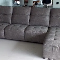 Szara, skórzana sofa modułowa z pikowanymi siedziskami i metalowymi nóżkami, ustawiona na jasnej podłodze w nowoczesnym wnętrzu.