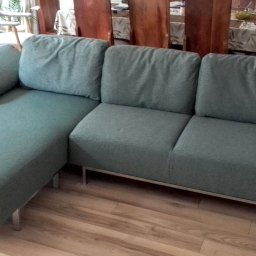 TOPMEBLE - MEBLE TAPICEROWANE ANDRZEJ ZALEWSKI - Turkusowa sofa z szezlongiem na metalowych nóżkach, widok z przodu, na drewnianej podłodze. W tle stół i krzesła, doniczki z roślinami.