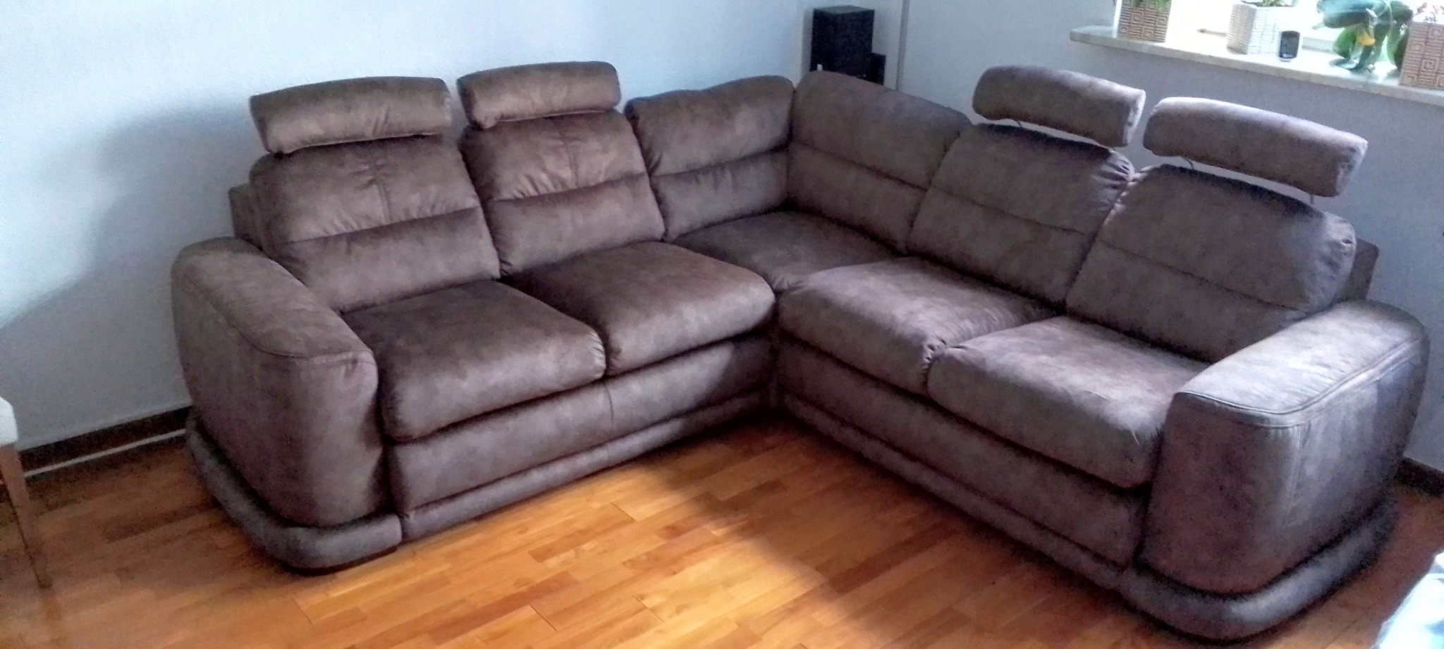 Brązowy narożnik z regulowanymi zagłówkami, ustawiony na parkiecie. Widoczne detale tapicerki i elementy dekoracyjne w tle, tworzące przytulną atmosferę.