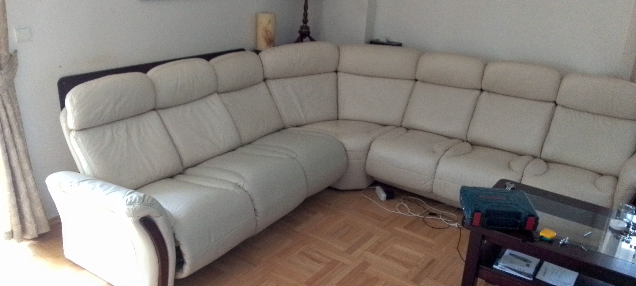 Jasny, skórzany narożnik z regulowanymi zagłówkami w salonie. Na stoliku narzędzia, sugerujące naprawę lub modyfikację. Parkiet na podłodze.