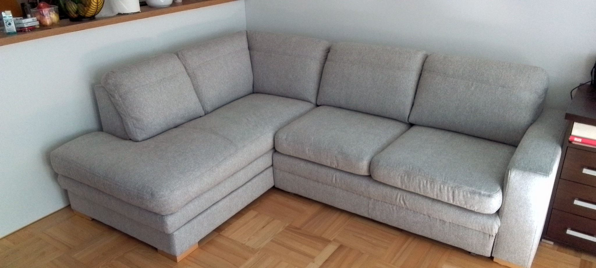 Jasnoszary narożnik tapicerowany z drewnianymi nóżkami, widoczny z perspektywy, na parkiecie. Minimalistyczny design, nowoczesny styl.