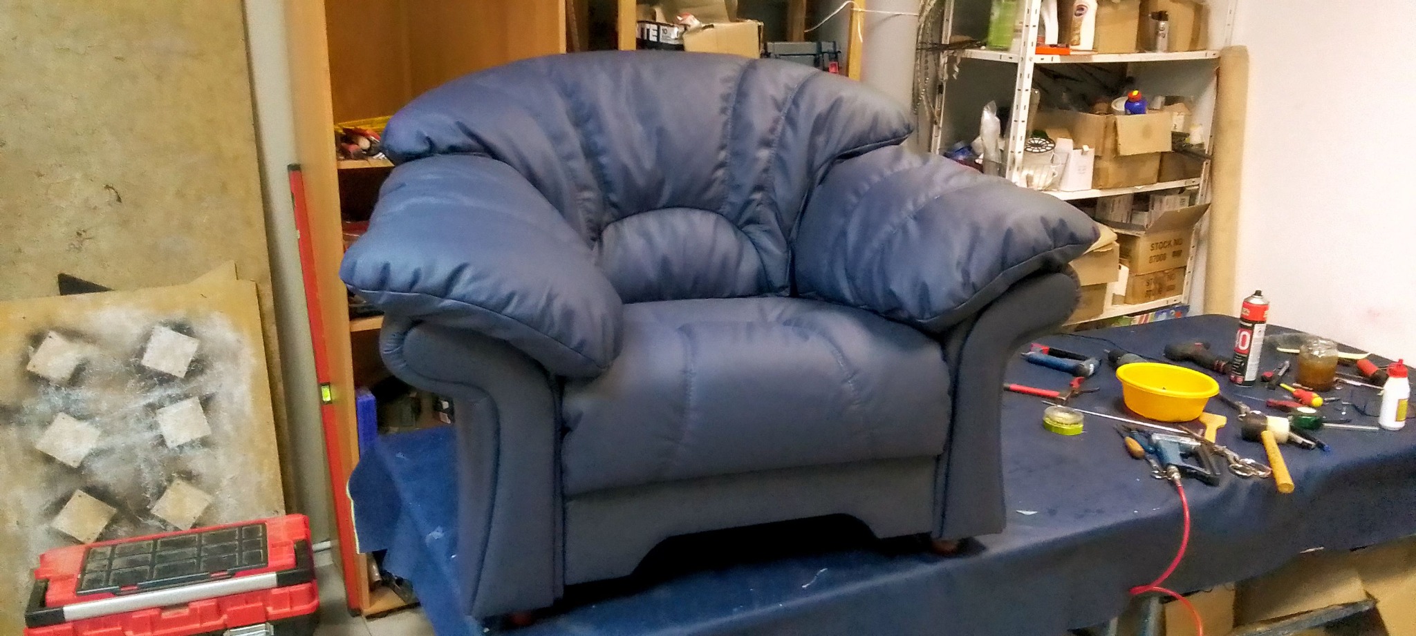 Granatowy fotel tapicerowany w warsztacie, otoczony narzędziami i materiałami. Widoczne detale szwów i wykończenia. Ujęcie z bliska, ukazujące fakturę tkaniny.