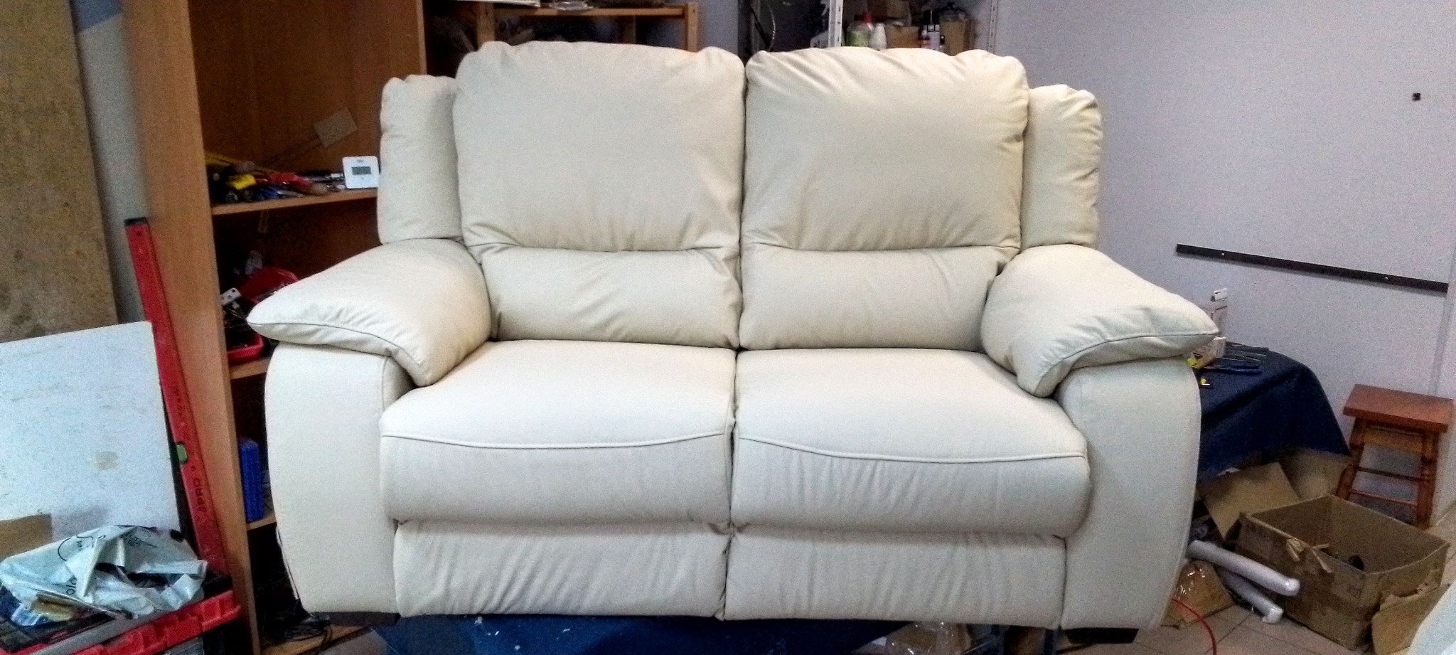 Jasna, dwuosobowa sofa z regulowanymi zagłówkami i podłokietnikami, widoczna z przodu, w warsztacie tapicerskim. Widoczne narzędzia i materiały w tle.