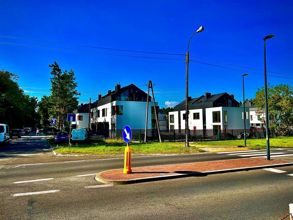 Nowoczesne, białe domy z czarnymi dachami widziane z perspektywy ulicy w słoneczny dzień, z widocznymi znakami drogowymi i liniami wysokiego napięcia.