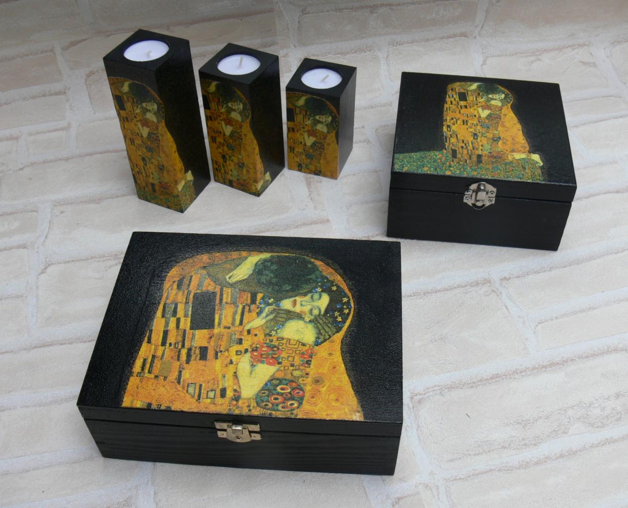 Ręcznie zdobione, czarne pudełka i świeczniki z motywem 'Pocałunek' Gustava Klimta na tle ceglanej ściany.