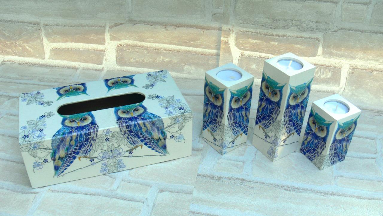 Biały pudełko na chusteczki i trzy świeczniki z motywem niebieskich sów i kwiatów, ustawione na tle ceglanej ściany.
